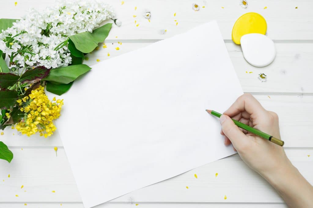 Mit Blumen dekorierter Tisch, leeres Blatt und eine Hand mit grünem Stift